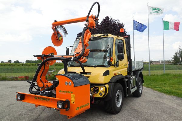Débroussailleuse à passage par-dessus ROAD-EAGLE MAXI UF Hymach pour Unimog, destinée à la tonte de l'herbe autour des poteaux de glissières de sécurité le long de la route.